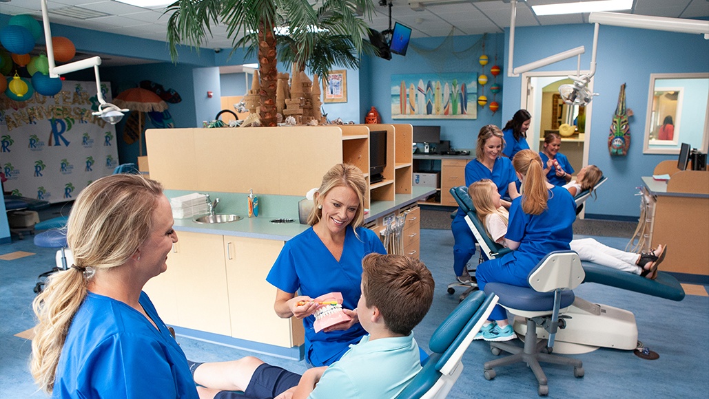 Team members helping young patients in a row of dental chairs